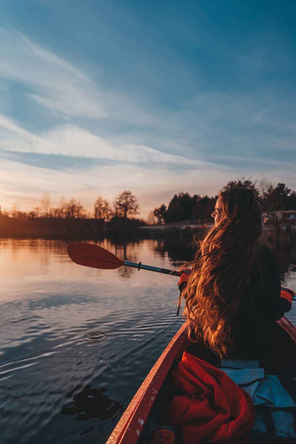 Back view of happy cute girl holding paddle in a kayak on the river